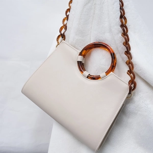 Détail de la chaîne épaisse en résine ambre et de la poignée sur un sac crème