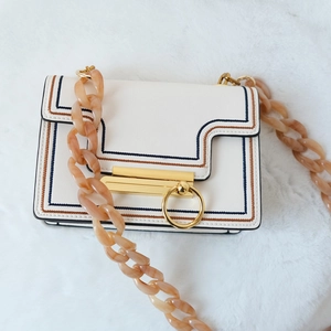 Détail du sac blanc rectangulaire avec chaîne épaisse en résine ambre et fermoir