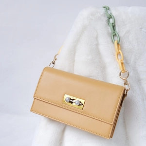 Close-up of golden metal clasp with two pearls and colorful resin chain on a ginger handbag