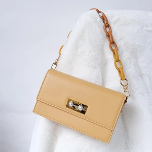 Detailed view of the yellow leather bag with pearl lock and chunky acrylic chain