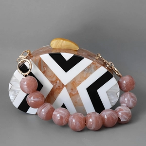 Detail einer Acryl-Clutch in Bernstein-Marmor mit geometrischem V-Muster und rosa Perlenkett