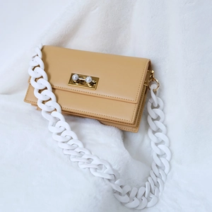 Close-up of brown leather handbag with thick white acrylic chain and pearl gold clasp