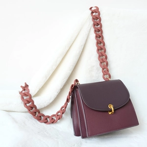 Detail of burgundy textured leather shoulder bag with thick matte pink resin chain strap
