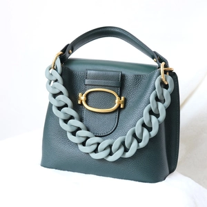 Close-up of dark green lychee leather handbag with gold lock and matte blue chain detail