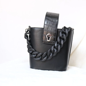 Chic black crocodile embossed bucket bag with matte chunky chain on plush white rug