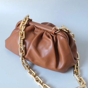 Sac nuage plissé marron avec une grosse chaîne en métal doré sur fond bleu clair