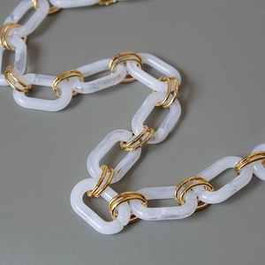 Macro detail of white marble acrylic rings and gold metal chain links for bags