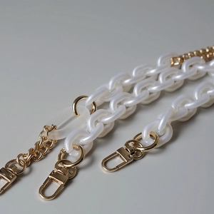Détail d'une bandoulière en résine nacrée blanche et métal doré avec des fermoirs mousquetons