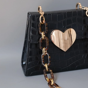 Detail of glossy black crocodile texture bag with gold heart buckle and amber resin chain