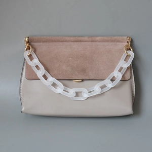 Detail of matte white acrylic chain on a two-tone crossbody bag with gold hardware