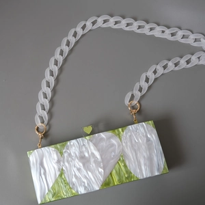 Détail de pochette en acrylique marbre vert avec patchs ovales et chaîne blanche givrée
