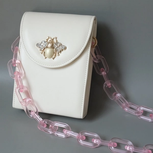 Detail of cream PU leather crossbody bag with gold bee buckle and pink acrylic chain