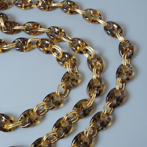 Macro detail of tortoiseshell resin links and polished gold rings for bag straps