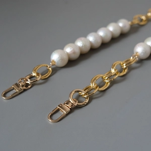 Detail of white pearls and golden metal rings with lobster clasp for bag straps