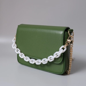 Détail d'un sac à main vert foncé mat avec chaîne acrylique blanche et bandoulière dorée