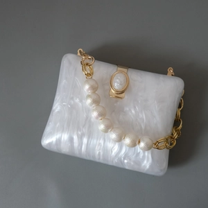 Detail of white marble acrylic clutch with gold hardware and pearl chain strap