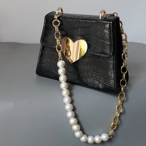 Detail view of black croc-embossed handbag with gold heart clasp and pearl chain strap