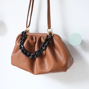Detail of a brown ruched cloud pouch bag featuring a thick black acrylic resin chain handle