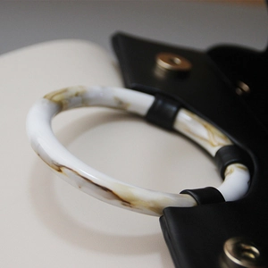 Detail of white marble resin handle attached to black leather bag with gold hardware