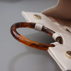 Close-up of amber resin round handle with tortoiseshell pattern on beige leather handbag
