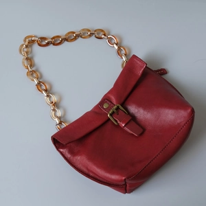 Detail of burgundy leather bag featuring amber resin chain and vintage brass buckle