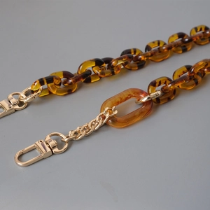 Detail of amber acrylic chain links mixed with gold metal strap and lobster clasp