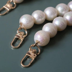 Macro shot of iridescent matte white pearls and light gold lobster clasps for handbags