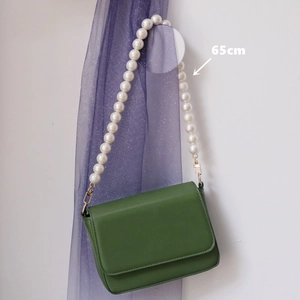Detail view of a green flap bag with a 65cm pearl chain strap and golden hardware