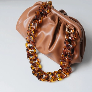 Detail of a brown leather pouch bag with thick amber resin tortoise chain strap