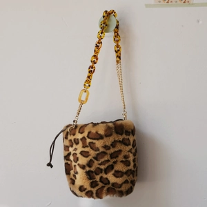 Detail of leopard print faux fur bucket bag with amber acrylic and gold metal chain