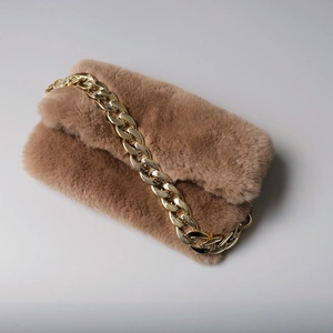 Detail of camel faux fur plush handbag with a chunky gold metal chain strap closeup