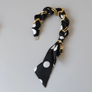 Close-up of black and white polka dot silk scarf entwined with golden metal bag chain