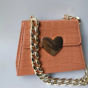 Detail of crocodile embossed brick red bag with gold heart clasp and thick chain strap