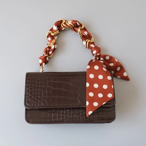 Detail of crocodile embossed leather handbag with silk scarf wrapped gold chain handle