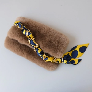 Close-up of golden chain strap woven with silk scarf on brown plush handbag