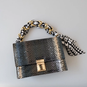 Detail of snake skin texture handbag with silk scarf wrapped around a golden chain strap