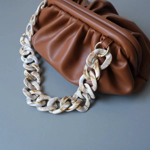 Detail of marble acrylic chain and gold rings on a pleated brown leather dumpling bag