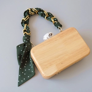 Detail of wooden clutch bag with golden chain handle and green polka dot silk scarf