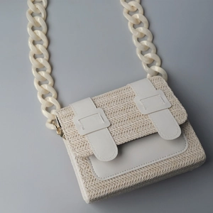 Detalle del bolso de paja trenzada con cadena de resina blanca y hebilla piel