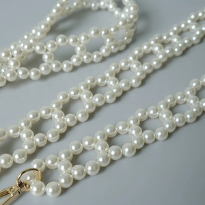 Detailed macro view of white pearl woven bag chain with gold metal lobster clasps