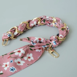 Close-up of pink floral silk scarf interwoven with gold chain and metal clasps