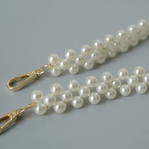 Détail de la chaîne de sac en perles blanches avec fermoirs dorés et tissage en spirale