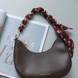 Detail of silk scarf wrapped around a gold chain handle on a brown crescent handbag