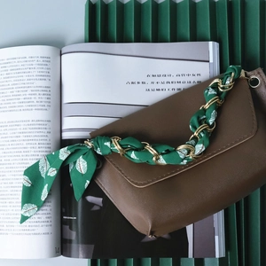 Detail of golden chain handle interwoven with green leaf print silk scarf on a brown bag