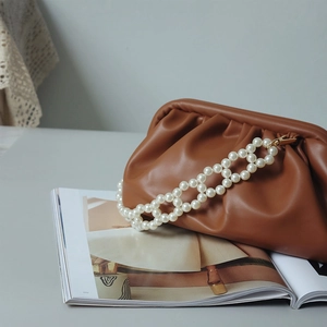 Close-up of brown pleated pouch bag with elegant double pearl chain strap on a magazine