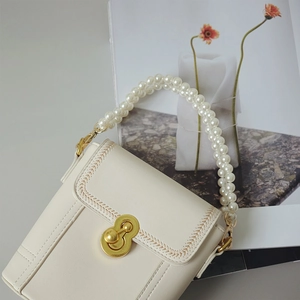 Close-up of white leather handbag featuring double pearl chain and golden metal twist lock