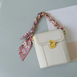 Detail of floral silk scarf woven through gold metal chain handle on cream handbag