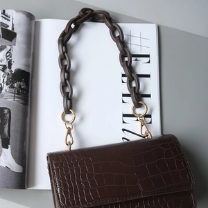 Brown crocodile embossed shoulder bag with chunky resin chain strap on a fashion magazine