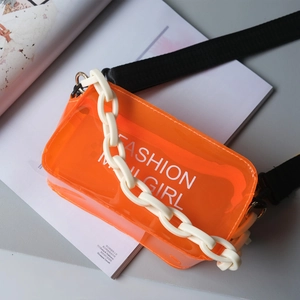 Orange transparent PVC mini crossbody bag with white acrylic chain on a magazine