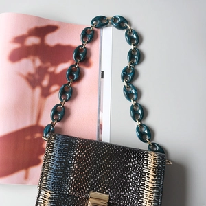 Detail of snake print textured handbag with bold green acrylic resin chain and gold hardware